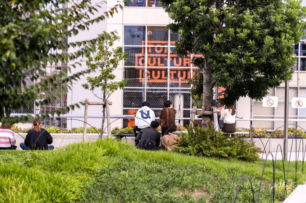 大草皮上坐著休息的人，遠處是寫著 CULTURE 的橘色牆面